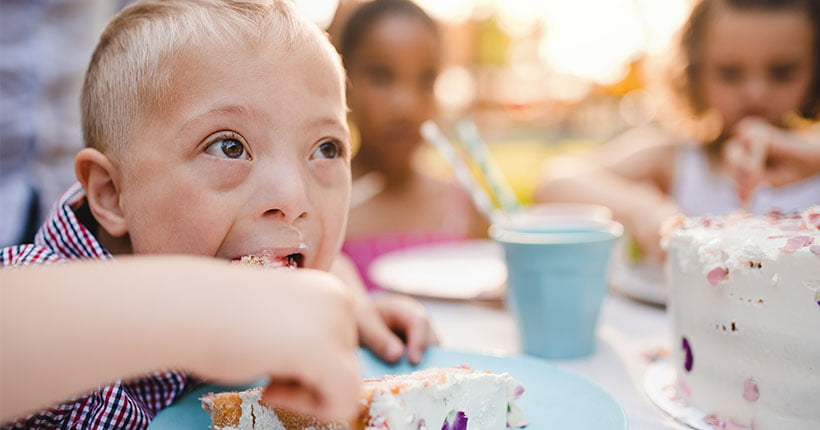 A boy with down syndrome at a party, eating cake