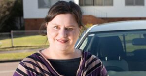 Hannah who has autism, standing outside in front of her car