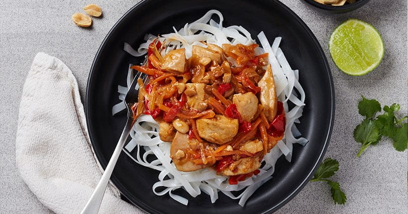 A bowl of pad Thai on a grey bench