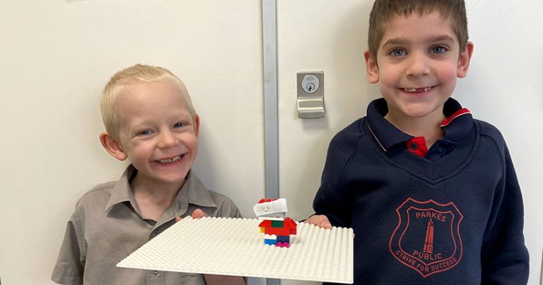 Two young boys smiling, holding up LEGO