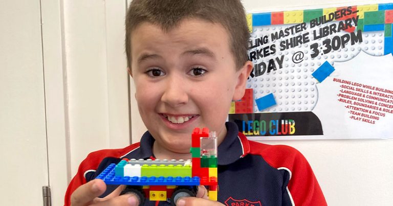 A young boy holds up a LEGO with an excited smile