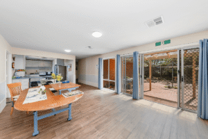 Open plan dining area with a table and chairs and glass doors to the backyard