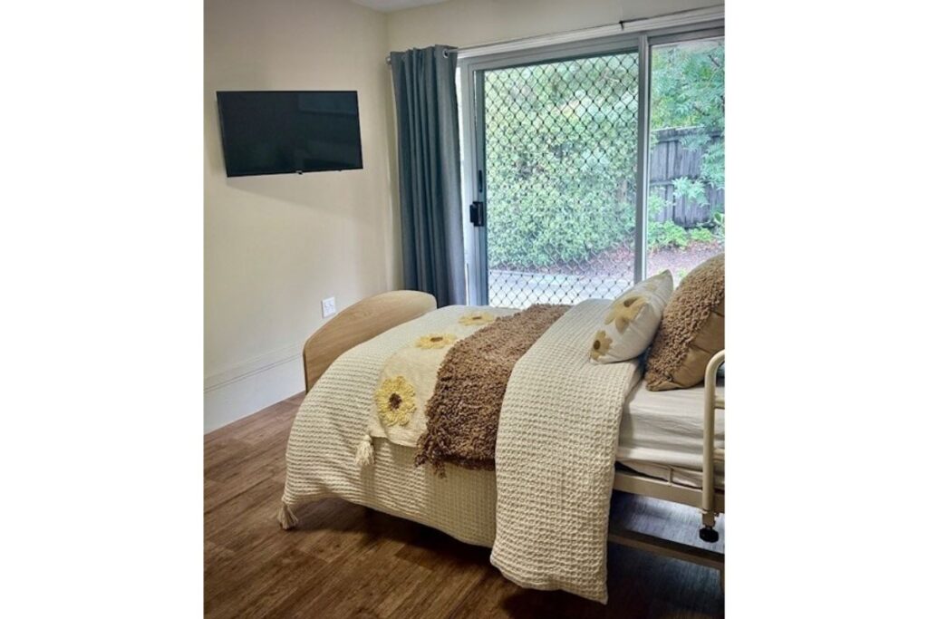 Bedroom with a made bed, wall-mounted TV and sliding door to the garden