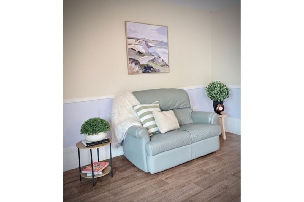 Sitting area with a grey sofa, cushions, a coastal artwork and a side table with a plant