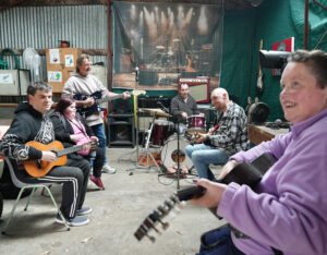 A group of Club Aruma participants playing guitars and drums together in a music session