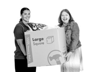 Two aruma participants smiling to the camera, holding a large moving box