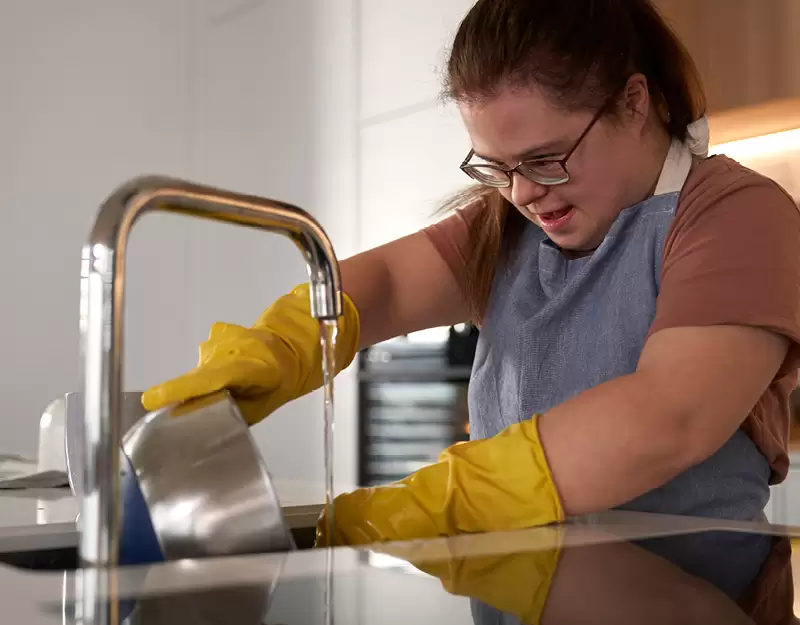 A woman washing dishes in her Specialist Disability Accommodation kitchen.