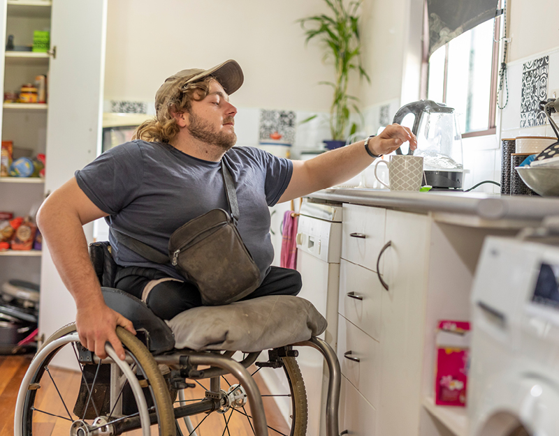 A man in a wheelchair making a cup of tea in his kitchen.