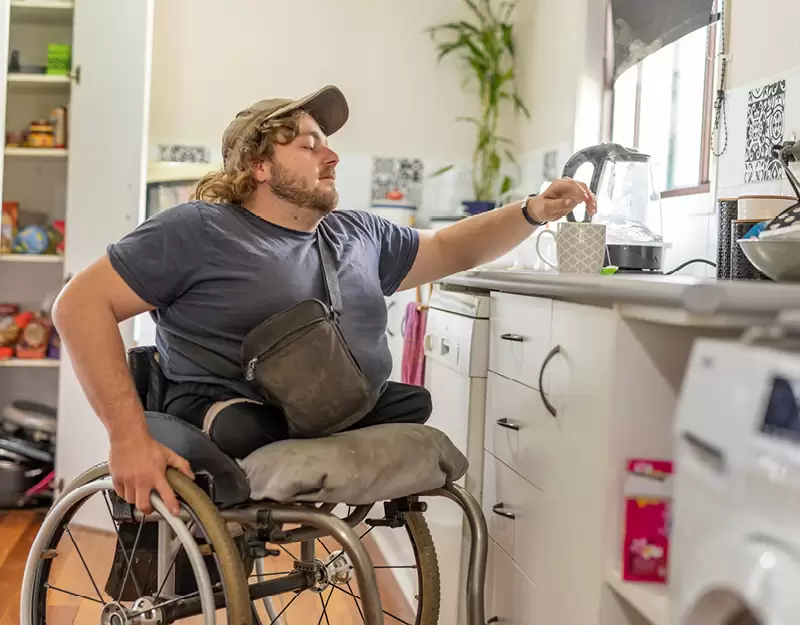 A man in a wheelchair making a cup of tea in his kitchen.