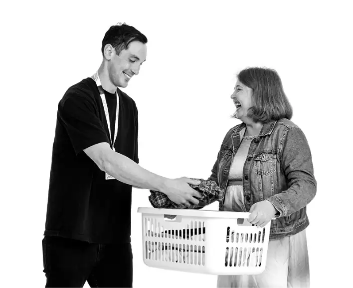 A support worker and participant laughing together while carrying a laundry basket during in home support