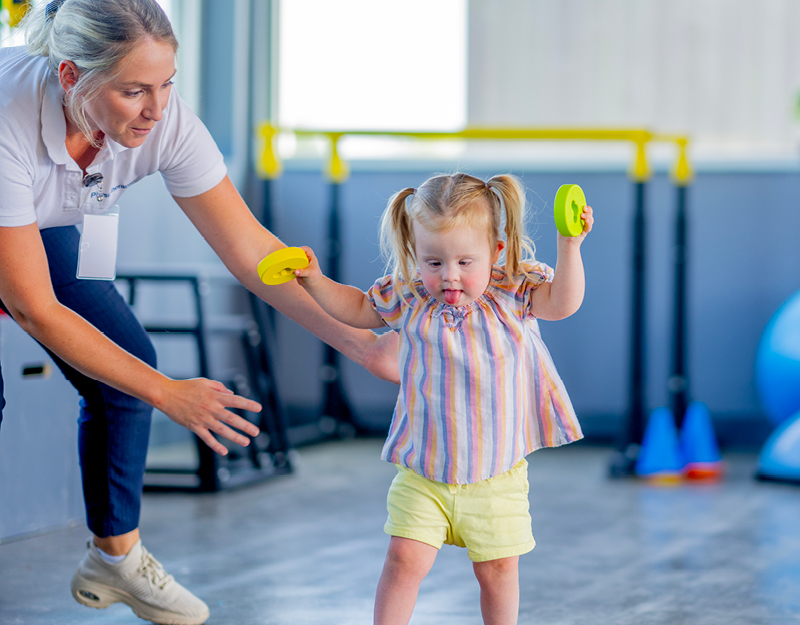 A therapist guiding a young girl holding colourful rings during an early childhood intervention therapy session