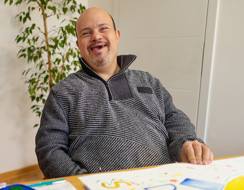 A man smiling while doing artwork at a table during an occupational therapy session for adults