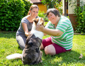 A support worker and participant sitting on the grass patting a dog during one-to-one community support
