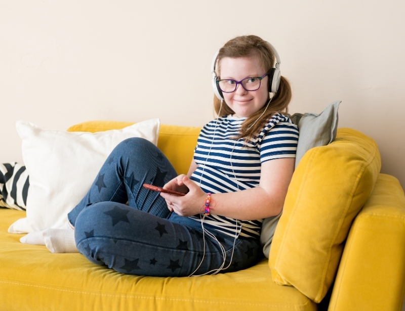 A young woman relaxing on a couch with headphones and a tablet during respite care for young people