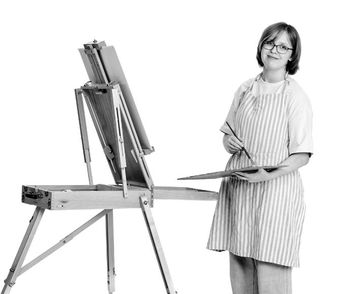 Emily standing at an easel holding a paintbrush and palette, ready to paint