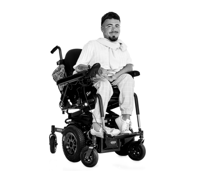 Tom sitting in his power wheelchair, smiling confidently