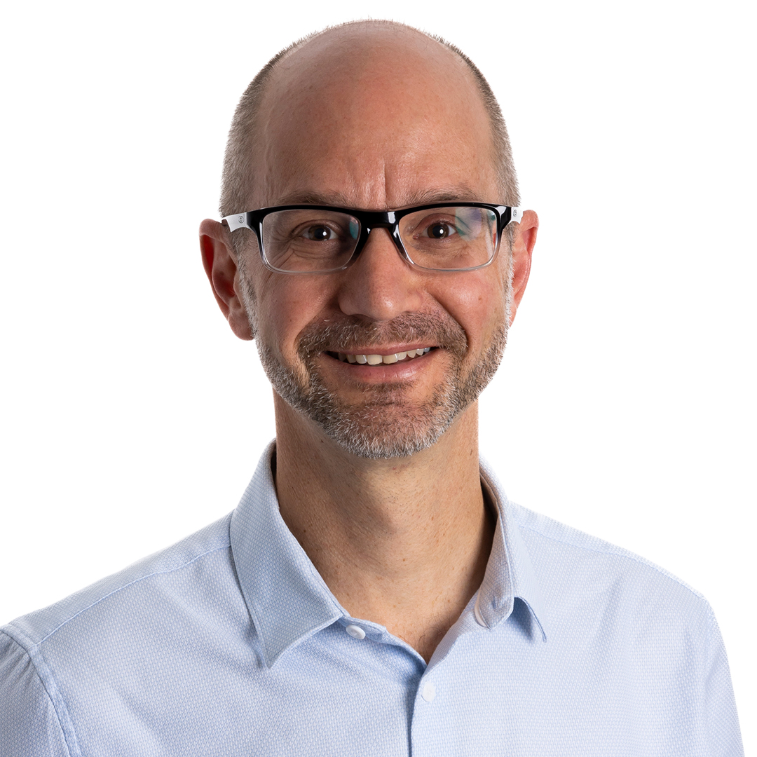 Darren Silber, Chief Finance Officer, smiling. He is wearing glasses and a light blue collared shirt, with a short beard and closely cropped hair.