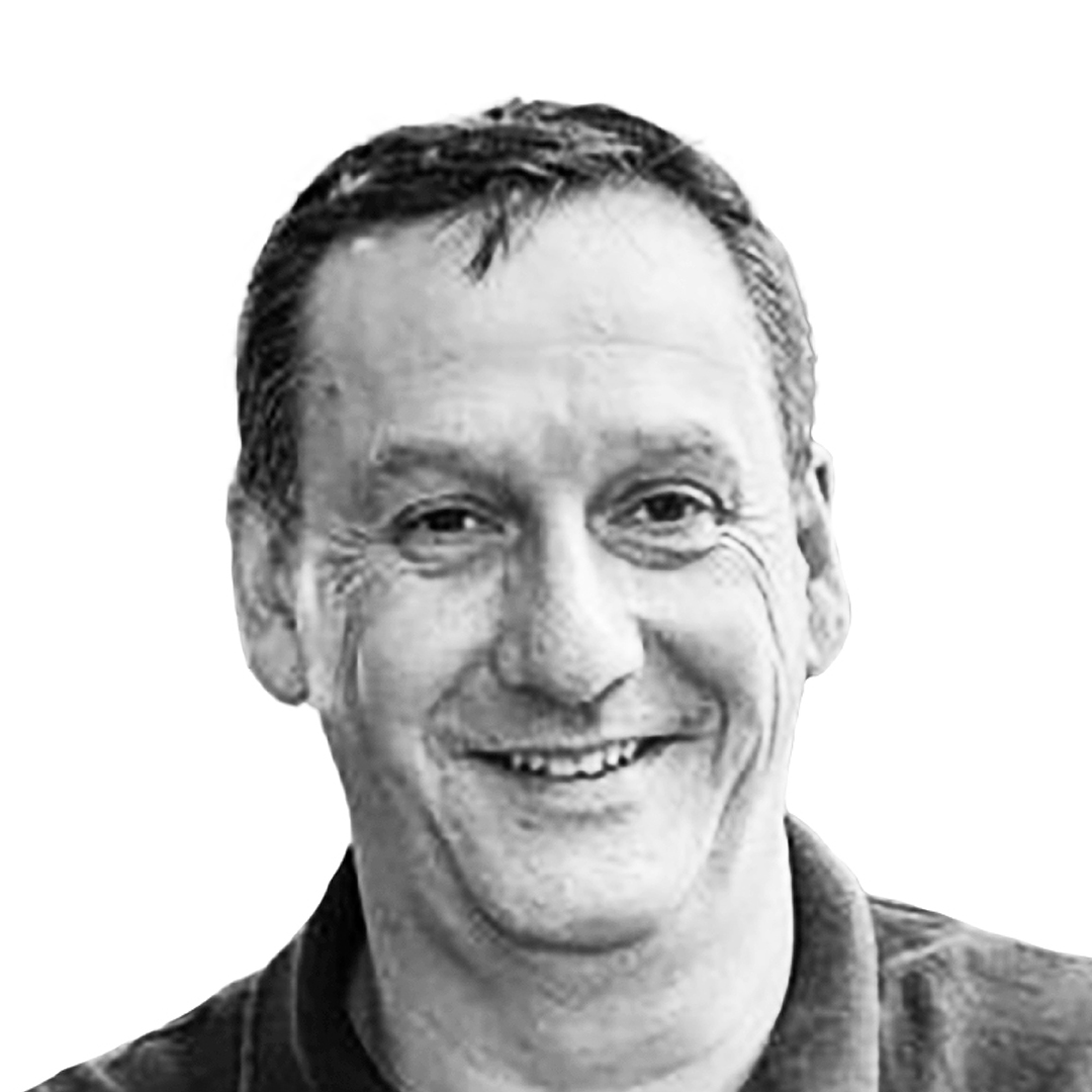 Black and white portrait of Malcolm Kinns, Chair, smiling. He has short greying hair and is wearing a dark casual shirt.
