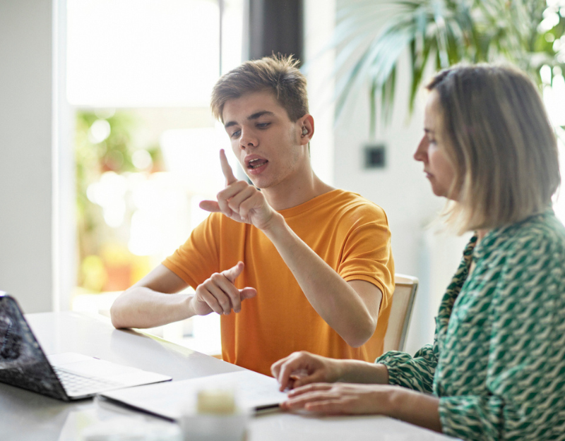 A young man using sign language while discussing ideas with a colleague, representing Aruma research