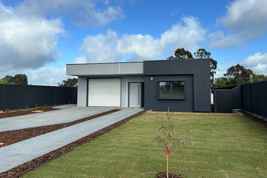 Front exterior of the second Long Gully SDA home, showing a matching single-storey modern home with dark grey and white cladding, garage, concrete driveway, mulch garden beds and grassed front yard.