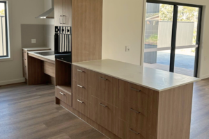 Kitchen inside one of the Long Gully SDA homes, showing timber cabinetry, stone benchtops with an accessible height section, built-in oven, induction cooktop and large windows looking out to the yard.