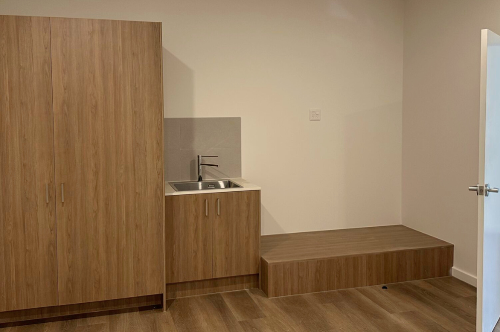 room inside one of the Long Gully SDA homes, showing a timber wardrobe, kitchenette with sink and a raised platform area.