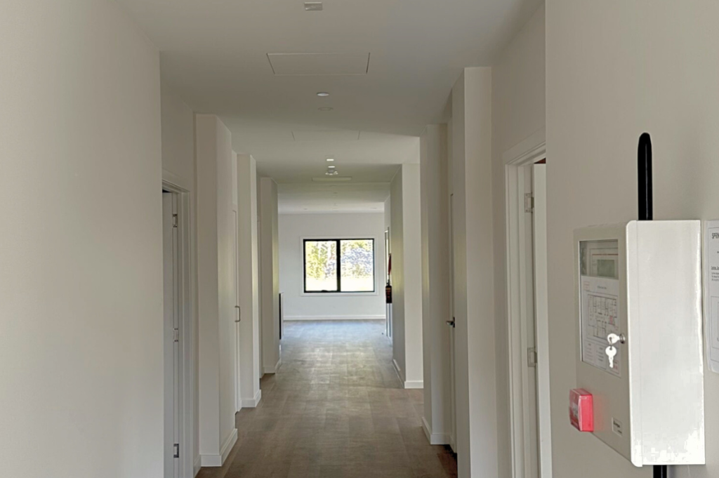 Wide hallway inside one of the Long Gully SDA homes, showing timber-look flooring, white walls, doorways to bedrooms and living areas and a fire safety panel mounted on the wall.