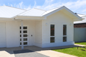 Close-up of the front entrance of the Mildura SDA home, showing the covered porch, front door with glass panels, large bay window and white weatherboard cladding.