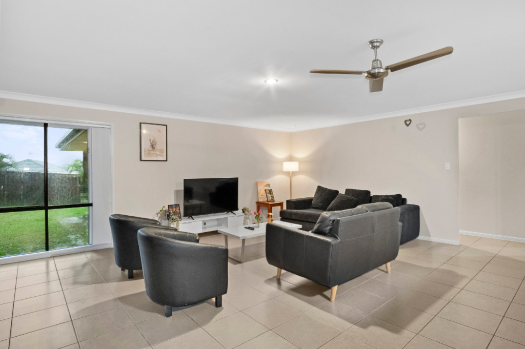 Living area inside the Pacific Pines SIL home, with lounge seating, a TV, ceiling fan and a sliding door to the backyard.
