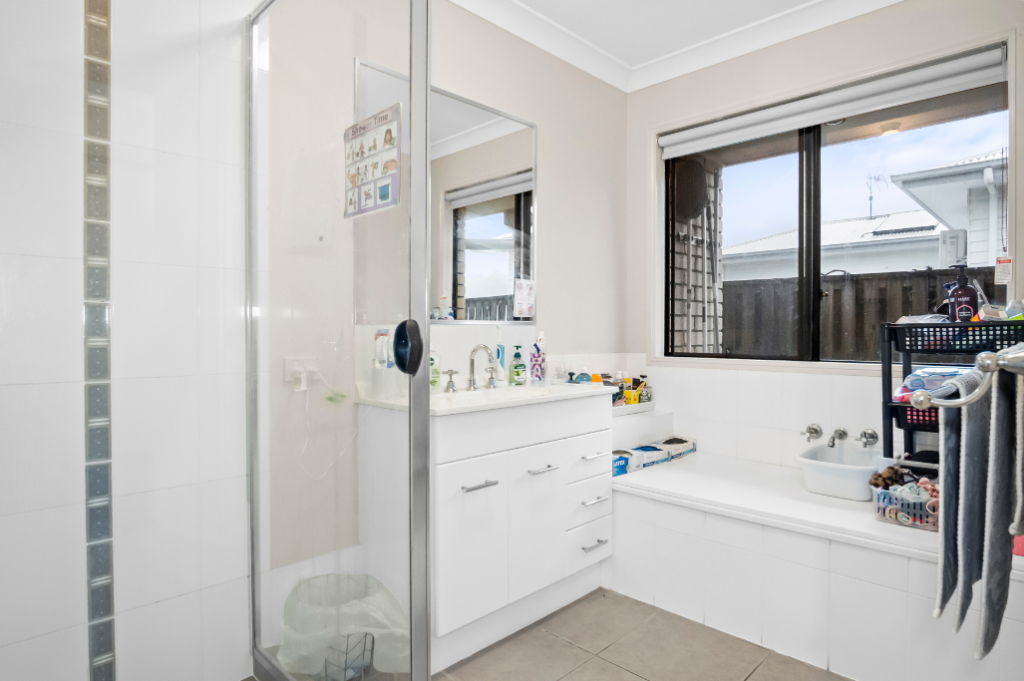 Bathroom inside the Pacific Pines SIL home, with a corner shower, vanity, bathtub and window.