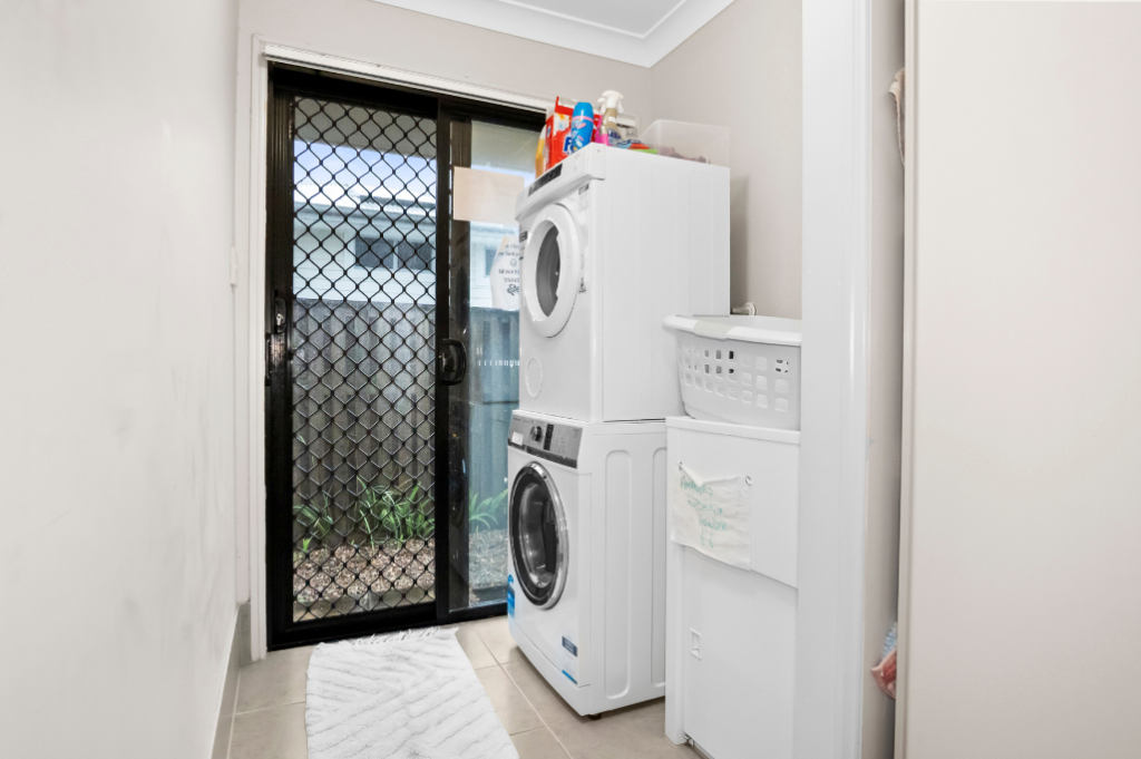 Laundry inside the Pacific Pines SIL home, with a stacked washer and dryer and a sliding door to the side of the home.