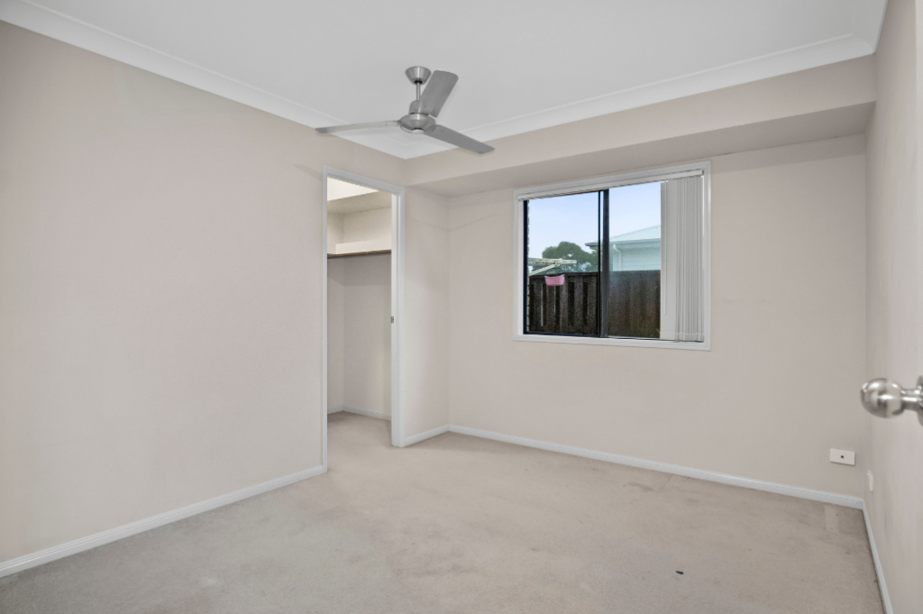 Vacant bedroom inside the Pacific Pines SIL home, with carpet, a ceiling fan, a window and a walk-in wardrobe.