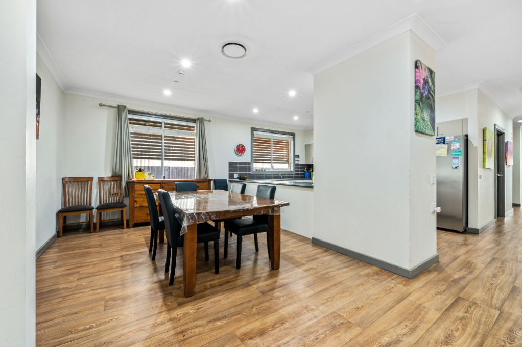 Dining area inside the Strathfield SDA home, showing a dining table with chairs, adjacent kitchen visible through an opening, artwork on walls and timber-look flooring.