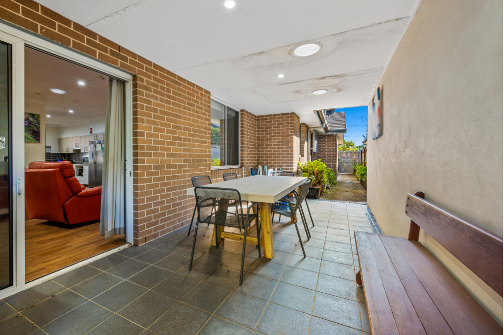 Covered alfresco area at the rear of the Strathfield SDA home, showing an outdoor dining table and chairs, bench seating, sliding door access to the living area and side access to the backyard.