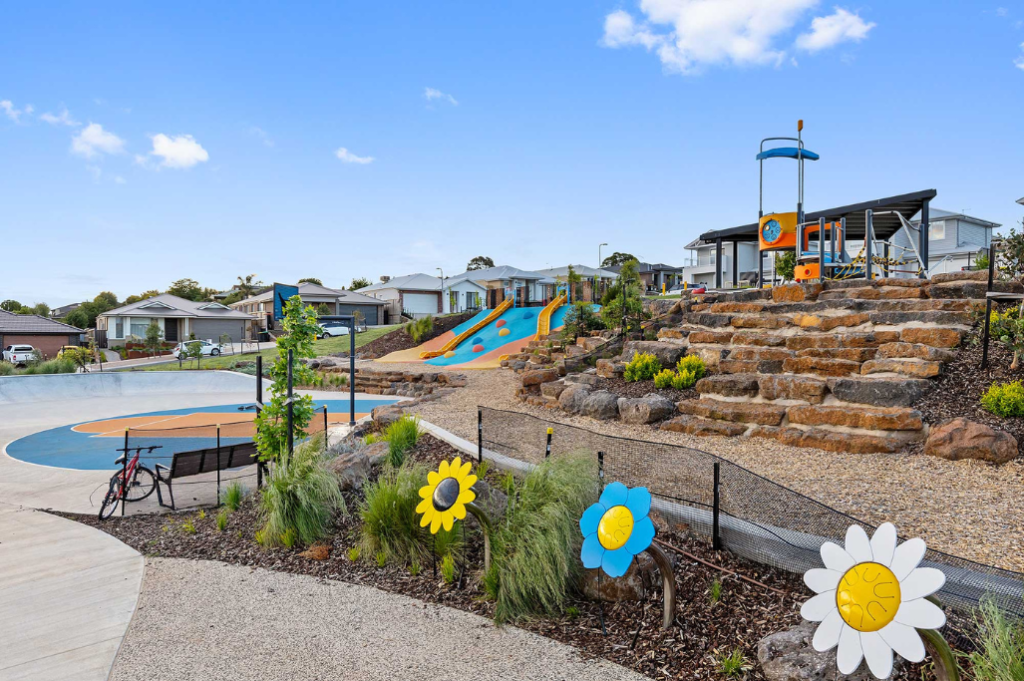 Local playground near the Sunbury SDA home, showing a colourful community park with slides, play equipment, decorative flower sculptures, pathways and surrounding residential neighbourhood.