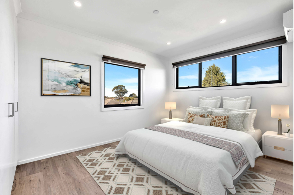 Bedroom inside the Sunbury SDA home, showing a double bed with bedside tables and lamps, artwork on the wall, wall-mounted air conditioning unit and windows with views of the surrounding neighbourhood.