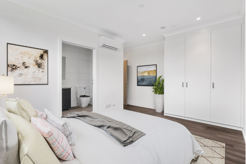 Second bedroom inside the Sunbury SDA home, showing a double bed, large built-in wardrobe, wall-mounted air conditioning unit, artwork and an ensuite bathroom visible through the open doorway.