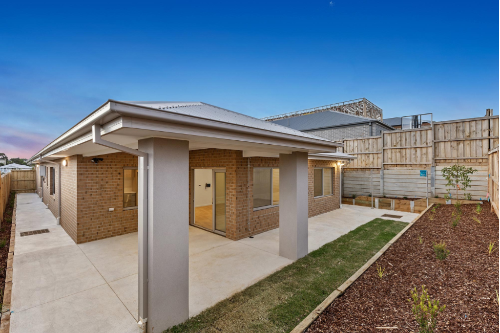 Rear exterior of the Sunbury SDA home at dusk, showing the covered alfresco area with sliding door access from the living area, brick facade, landscaped backyard with lawn and new garden plantings.