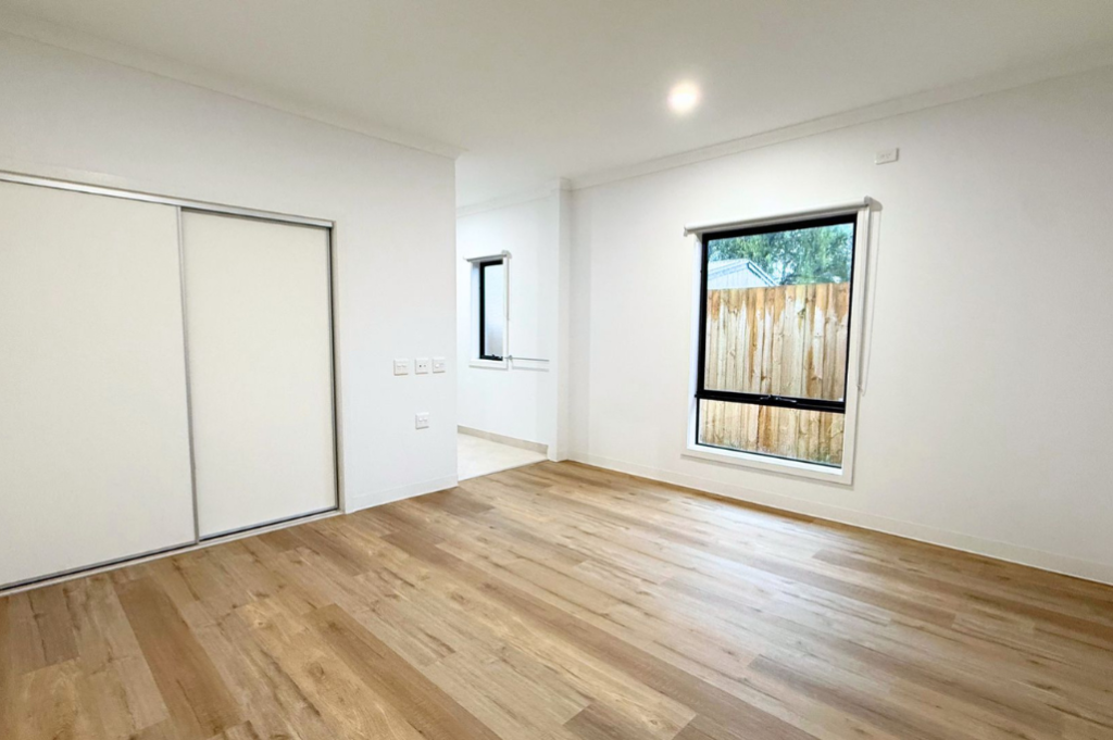 7. Bedroom inside the Sale SDA home, with built-in sliding wardrobe, large window and timber-look flooring.