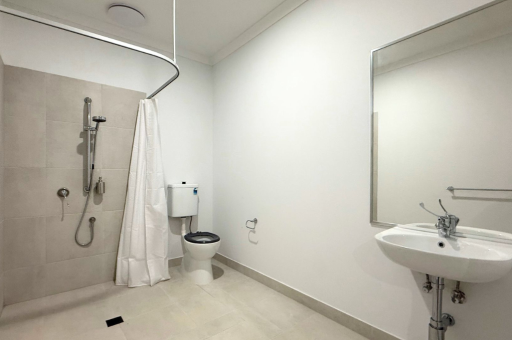10. Accessible ensuite inside the Sale SDA home, with roll-in shower and curtain rail, accessible toilet and wall-mounted basin with mirror.