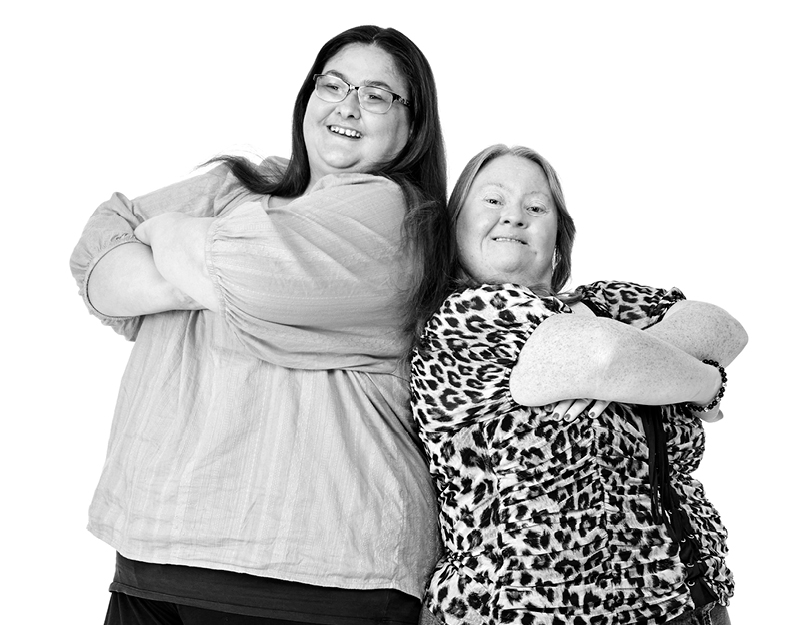 Two women smiling standing back to back. They are house mates in an Aruma SIL.