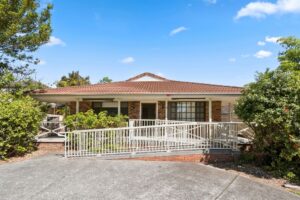 Front exterior of the Albion Park SIL home, a single-storey brick house with a tiled roof, covered front verandah and accessible ramp leading to the front entry.