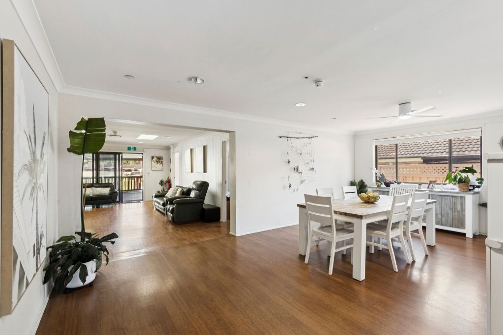 Open shared living and dining area inside the Albion Park SIL home, with timber-look flooring, a large dining table, lounge seating and a ceiling fan.
