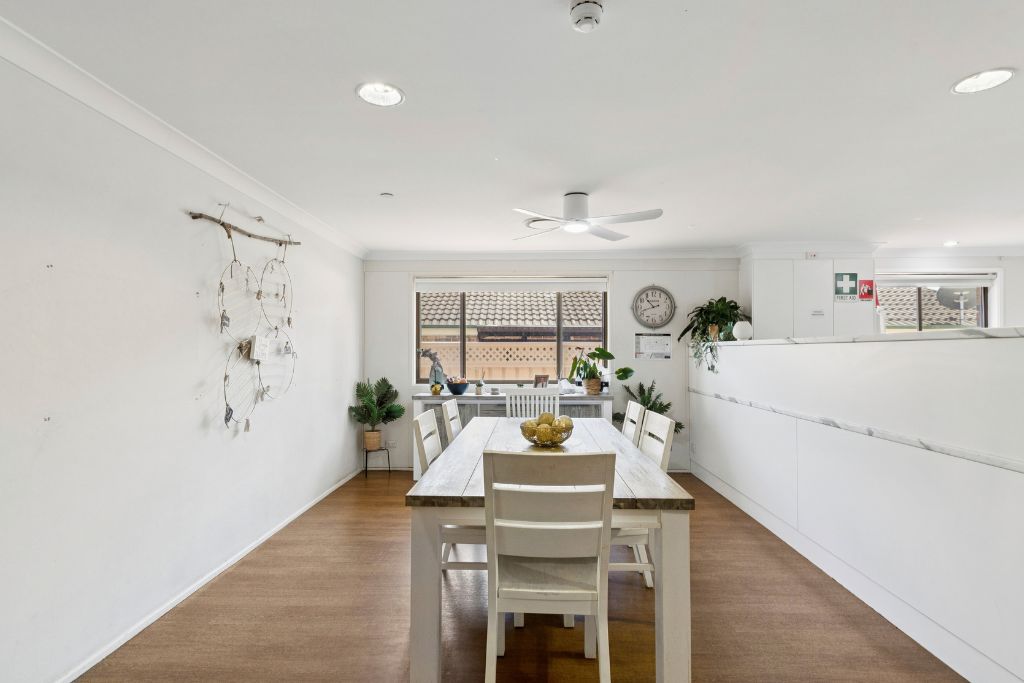 Dining area inside the Albion Park SIL home, with a large timber dining table, ceiling fan and a window looking out to the yard.