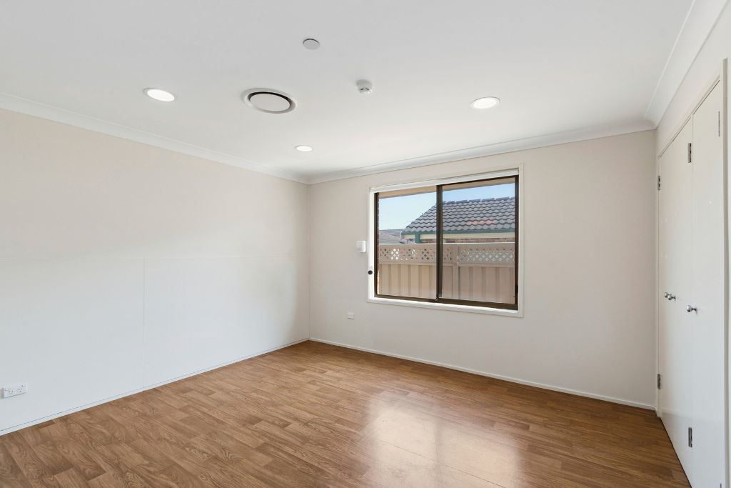 Vacant bedroom inside the Albion Park SIL home, with laminate flooring, a built-in wardrobe and a window overlooking the yard.