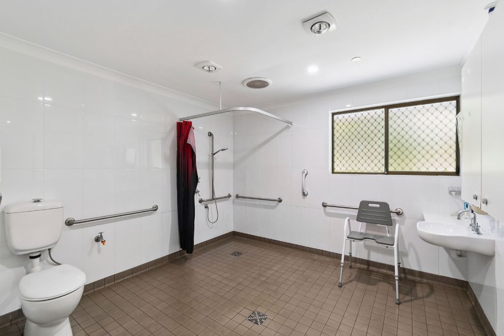 Accessible bathroom inside the Albion Park SIL home, with a walk-in shower with grab rails and shower seat, wall-mounted basin and accessible toilet.