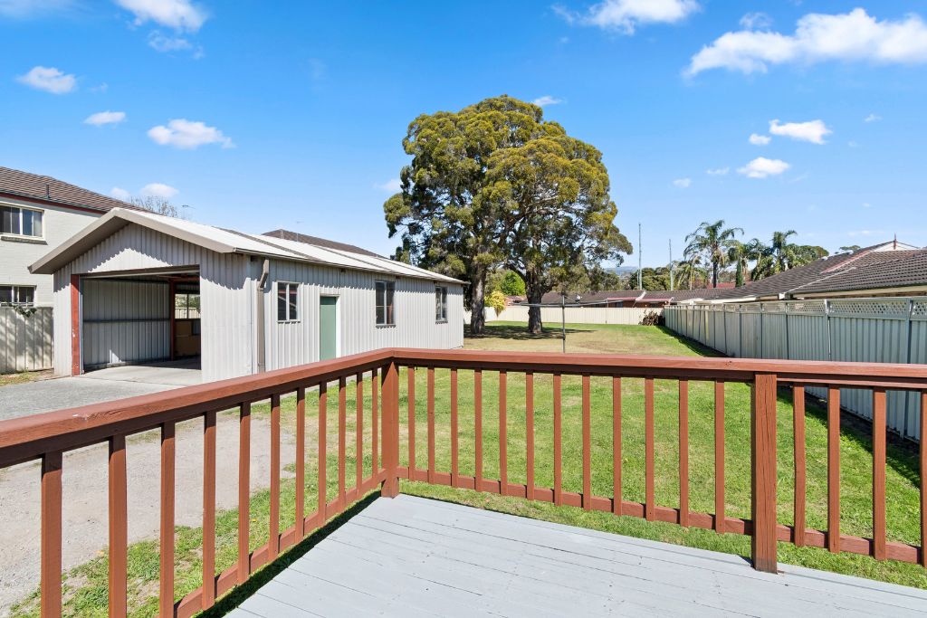 Fully fenced backyard of the Albion Park SIL home, a large grassed area with mature trees and a detached shed at the rear of the block.