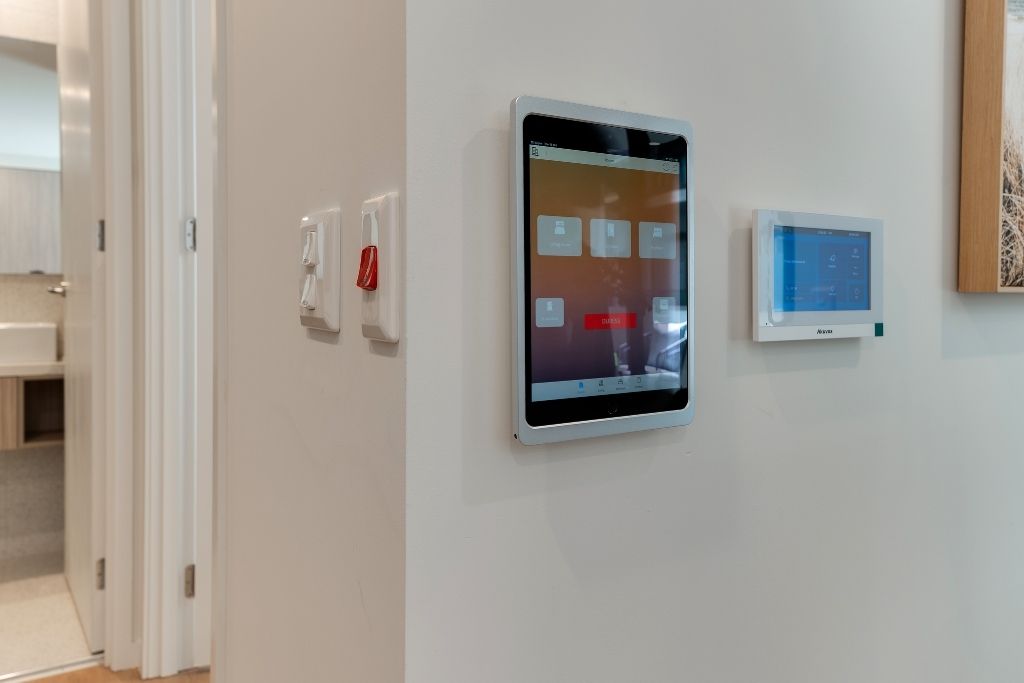 Smart home automation panel inside the Essendon SDA apartment, mounted on the wall alongside light switches and an emergency call button.