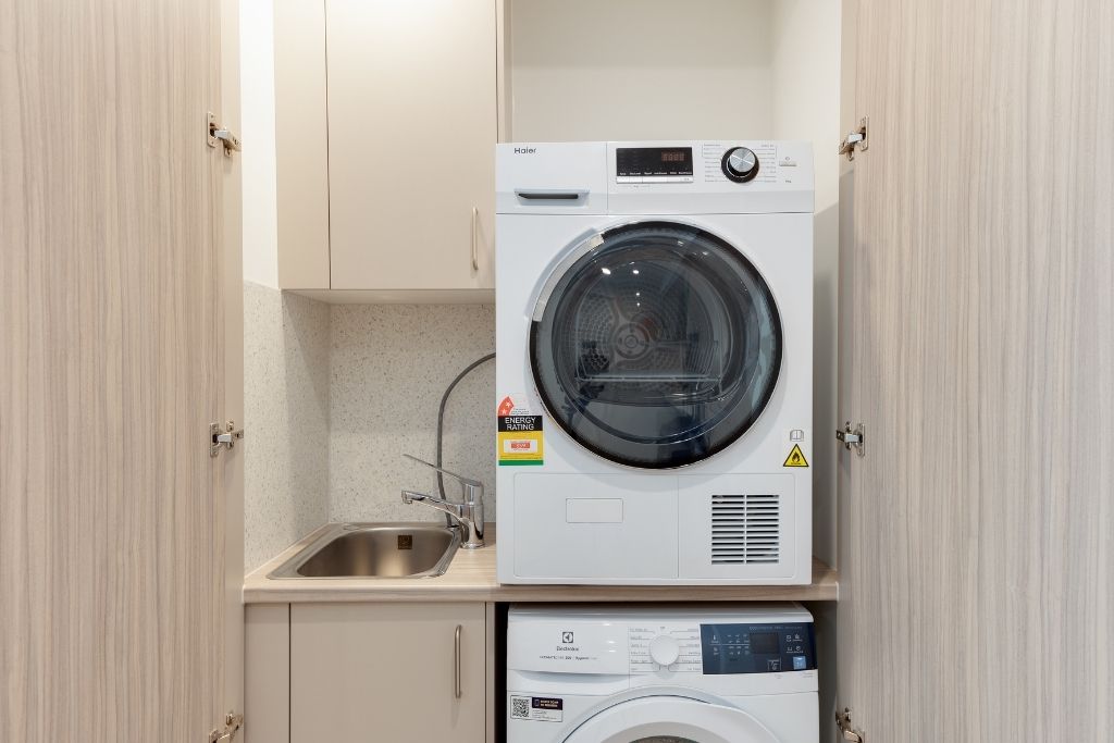 Laundry inside the Essendon SDA apartment, showing a stacked washer and dryer, sink and cabinetry.