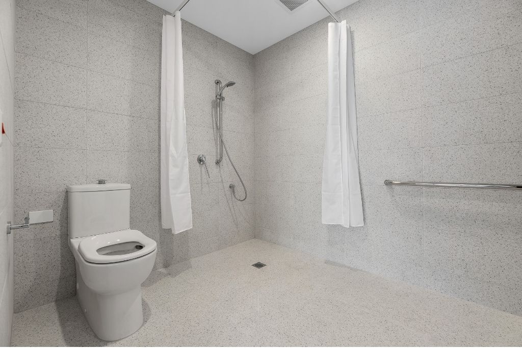 Accessible bathroom inside the Essendon SDA apartment, showing a roll-in shower with grab rails, accessible toilet and wide tiled circulation space.